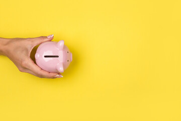 Woman holding a  piggy bank on a yellow desk