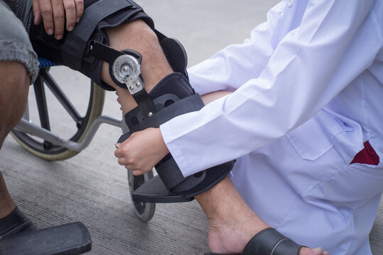 Female Physiotherapist Fixing Knee Braces On Man's Leg In Out Door, Image Of Doctor Putting On Knee Brace To Asian Patient, Health Concept.selective Focus