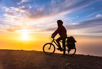 Mountain bicycle rider with backpack travels over sunrise background, Lanzarote Canary Island