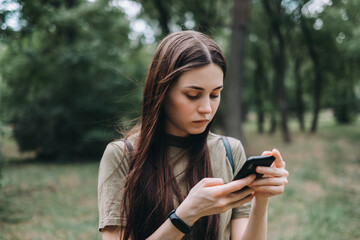 Excited young woman in the city park alone, use a smartphone and typing text.