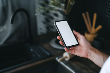 Man using a smartphone with a white blank screen in the kitchen. 