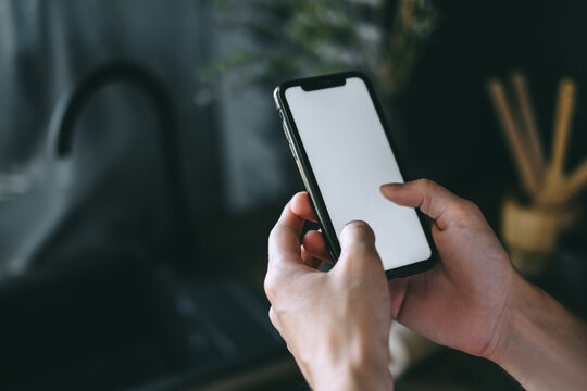 Man using a smartphone with a white blank screen in the kitchen. 