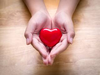 Hands of child holding a red heart on a wooden table for love and concern of all family members. Adoption foster family, romance, healthy and valentine day concept.