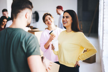 Charming attractive female hipsters talking with male coworker joking and having fun while making preparation for designing office indoor collaborating and helping each other in friendly atmosphere