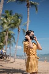 Asian woman wearing protective face mask on the beach,  newnormal lifestyle after Coronavirus pandemic.