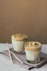 Dalgona whipped coffee, instant, cream, iced coffee. Cocktail with coffee, milk and ice cubes on light beige background mockup. Trendy drink background with copy space for text.