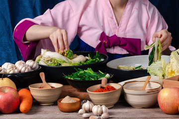 Asian women wearing Korean traditional costumes (hanbok) are mixing fresh stir-fry and kimchi...