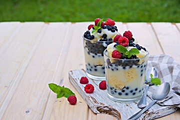 Dessert, truffle with biscuit, fresh blueberries, raspberries and custard or cream in glasses on a light background. Desserts recipes with berries, blueberries. British cuisine.
