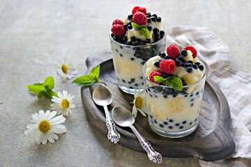 Dessert, truffle with biscuit, fresh blueberries, raspberries and custard or cream in glasses on a light background. Desserts recipes with berries, blueberries. British cuisine.