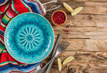 Festive Mexican table setting. Plate and cutlery with colorful napkin on rustic wooden background....