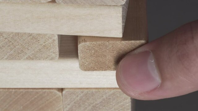 Male fingers take wooden piece from Jenga game tower close up