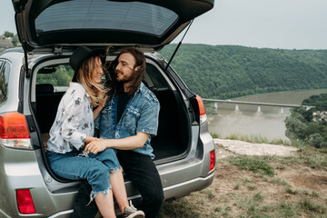 Young Stylish Traveling Hipsters Having Fun Sitting in Car Trunk Near the River Canyon, Travel and Road Trip Concept