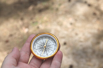 Old classic navigation compass in hand on natural background as symbol of tourism