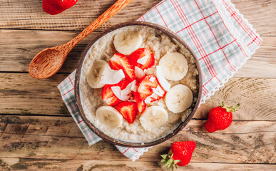 Quinoa porridge with coconut milk and fresh strawberries in a coconut bowl wooden rustic background. Healthy Lactose and Gluten Free Breakfast.