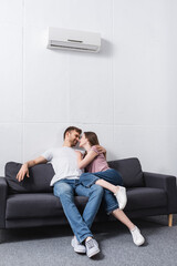 smiling girlfriend and boyfriend hugging and looking at each other at home with air conditioner