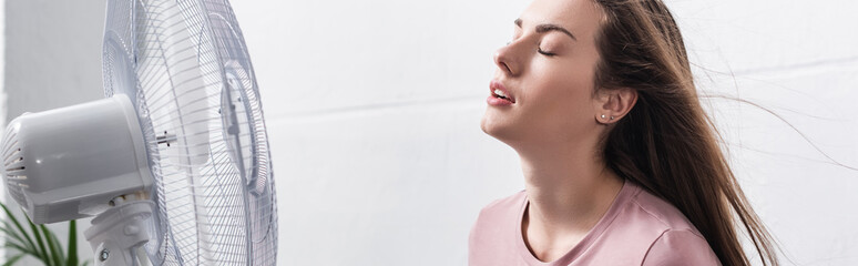 beautiful woman feeling comfortable with electric fan during summer heat, website header