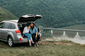 Young Stylish Traveling Hipsters Having Fun Sitting in Car Trunk Near the River Canyon, Travel and Road Trip Concept