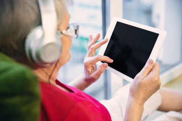 Mature woman spending time being quarantined - caucasians woman using modern gadgets, drinking tea. Eyes tired of gadget's using. Interested and having fun. Copyspace on blank screen. Lifestyle.