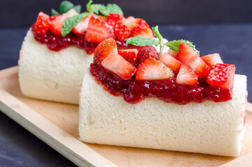 Delicious home made cake roll with strawberry marmalade jam in japanese style  on a wood plate with topping  fresh strawberry , strawberry marmalade jam and mint. Tasty dessert.