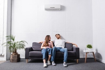 young couple suffering from heat while sitting home with broken air conditioner