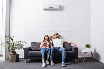 Obraz premium young sad couple suffering from heat while sitting home with broken air conditioner