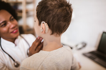 Fototapeta premium Smiling deaf boy with ear implant at doctor's office.