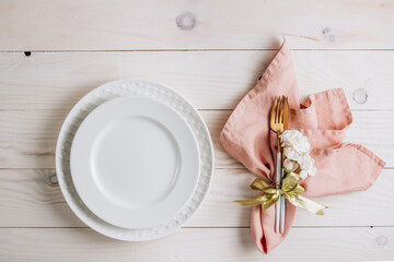 Festive table setting. Plates and cutlery with pink napkin on white wooden background. Beautiful flat lay arrangement. Top view