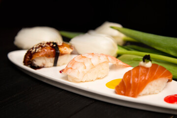 Set of Japanese Nigiri Ebi Sushi with tiger shrimp in focus near nigiri Sake with salmon and Unagi with eel. colourful food decoration painting spots on plate near white tulips. Asian restaurant menu
