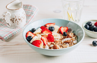 Healthy breakfast bowl with oat granola with dried buckwheat, nuts and coconut chips, berries and rice milk on a white background. Selective focus