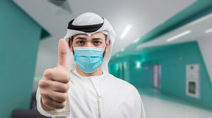 Fototapeta na wymiar Young man in sterile face mask posing in clinic background. Epidemic pandemic rapidly spreading coronavirus 2019-ncov sars covid-19 flu virus concept. Showing thumbs up