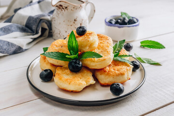 Trandy homemade food - fluffy mini pancakes with blueberries and mint on a white wooden background. Selective focus