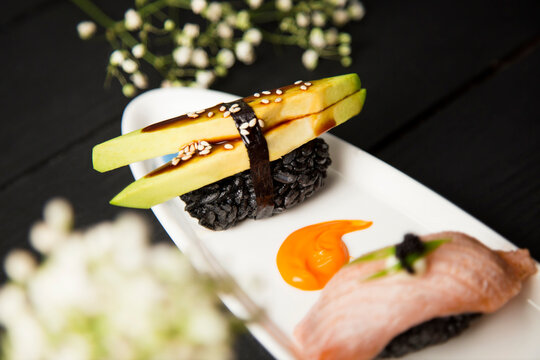 Japanese Nigiri Sushi with avocado, sesame seeds and Unagi sauce in focus on white plate decorated with colour paints. food decoration. Pan Asian seafood restaurant menu cuisine concept with flowers
