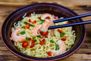Instant noodle with shrimps, red pepper and green onion in a ceramic bowl. Japanese food. Chopsticks with shrimp
