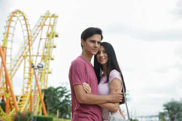 Happy Caucasian young couples hug and stand together at theme park on Roller coaster background