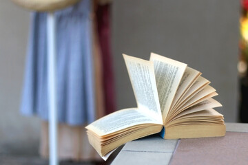 Open book in a room, clothing rack in the background. Selective focus.