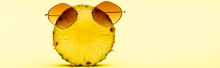 delicious sweet cut pineapple in sunglasses on yellow background, panoramic shot