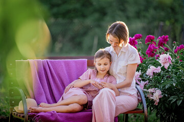 Happy family relationships. Mom and daughter sit on a bench and chat in the garden among the flowers on a sunny summer evening.
