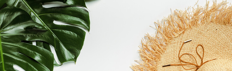 top view of green palm leaves, straw hat on white background, panoramic shot