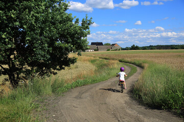 Mała dziewczynka jedzie na rowerze polną drogą przez pola.