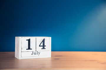 July 14 - white calendar blocks on wooden table against vintage blue background