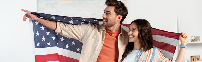 Panoramic crop of smiling man pointing with finger while holding with girlfriend american flag