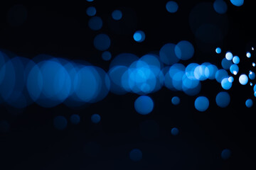 Bokeh of water drops reflects light connected horizontally on a black background. Abstract defocused dark blue background.