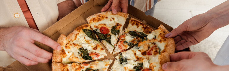 Panoramic shot of friends holding pieces of tasty pizza at home