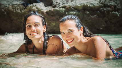 Two beautiful woman friends lying in shallow tropical sea
