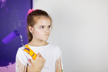 Repair in the apartment. Happy child girl paints the wall