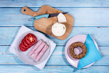 Breakfast served at blue wooden table with juice, ham, pecorino cheese, tomato and corn bread pretzel. Continental delicious healthy breakfast table - top view