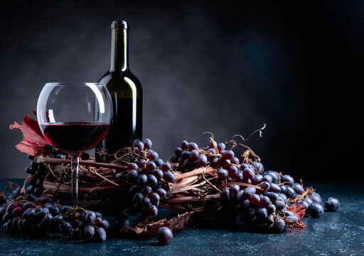 Bottle and glass of red wine and blue grapes on a dark blue background.
