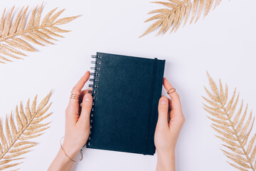 Female hands holding black notebook among golden palm branches