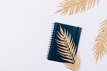 Black notebook with golden palm leaves on white desktop
