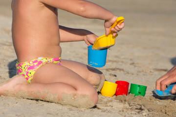 Fototapeta na wymiar A little child plays in the sand on an ocean beach. Relax on the beach by a happy family.